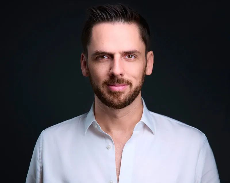 Corporate headshot of a man in a white shirt on a dark studio backdrop
